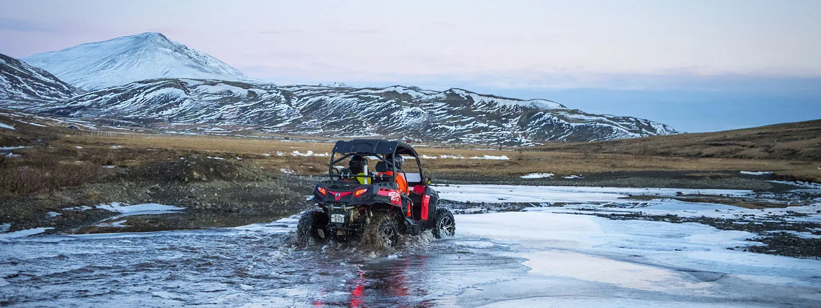 Buggy crossing a shallow river below snowy mountains